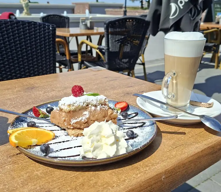 Deser z bitą śmietaną i owocami obok kawy latte